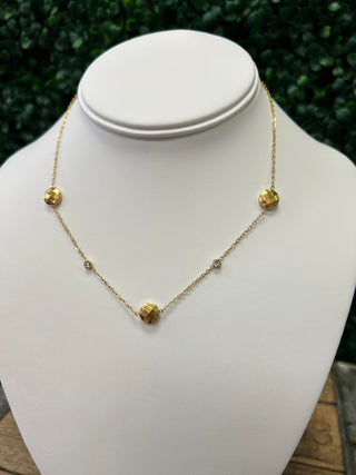 Gold chain necklace with faceted disc charms and crystal accents displayed on white jewelry bust