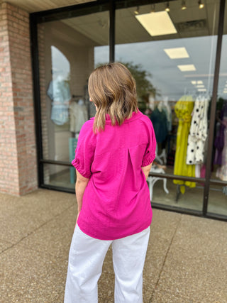 Woman wearing bright pink collared blouse and white pants, standing outside storefront window shopping