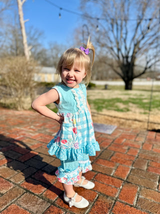 Young girl wearing light blue floral dress with matching ruffled leggings standing on brick patio outdoors