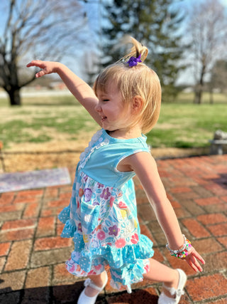 Young girl dancing outdoors wearing colorful floral dress with ruffled layers and matching hair accessory.