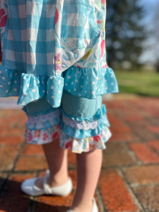 Young girl wearing colorful ruffled dress with mixed patterns including gingham, polka dots, and floral prints.