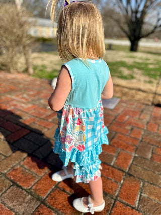 Young girl wearing turquoise sleeveless top with floral ruffled skirt walking on brick pathway outdoors.