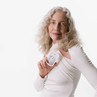 Woman in white holding Touchland Rainwater Power Mist hand sanitizer against clean white background.