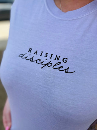 Light purple t-shirt featuring "RAISING disciples" embroidered text in black lettering on chest area.
