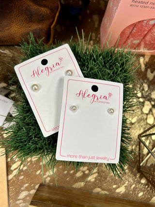 Two pairs of freshwater pearl stud earrings on Alegria Accessories branded cards with festive greenery decoration.