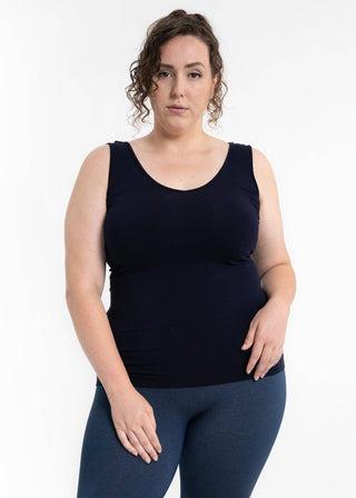 Woman wearing navy sleeveless reversible cami top with blue leggings against white background