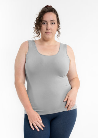 Woman wearing gray reversible cami tank top with blue leggings against white background