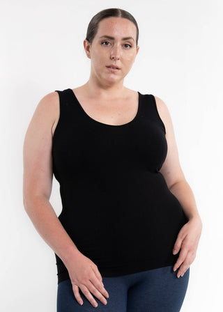 Woman wearing black sleeveless camisole top with blue jeans against white background