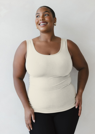 Woman wearing cream-colored reversible camisole tank top, smiling and looking upward against white background.