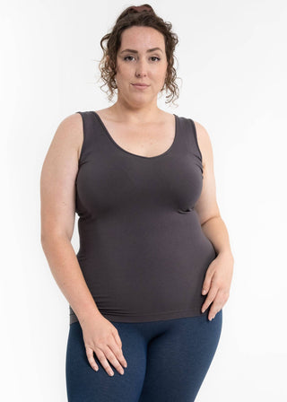Woman wearing dark gray reversible cami tank top with blue leggings against white background