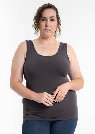 Woman wearing dark gray sleeveless tank top with hands positioned at waist against white background.