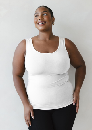 Woman wearing white reversible cami tank top, smiling and looking upward against neutral background.