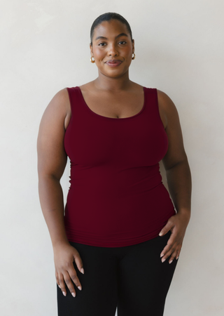 Woman wearing burgundy reversible tank top with black pants against neutral background
