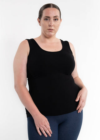 Woman wearing black sleeveless reversible cami top with blue leggings against white background.