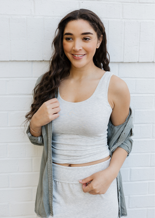 Young woman wearing gray reversible cami top with matching cardigan against white brick wall background.