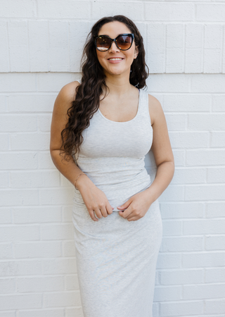 Woman wearing light gray fitted sleeveless dress with sunglasses against white brick wall.