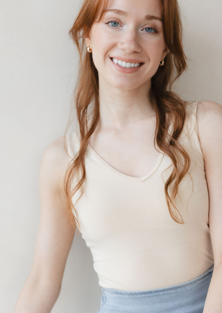 Woman wearing beige reversible cami top with wavy hair and gold earrings smiling