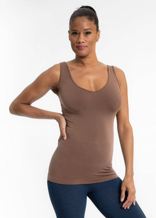 Woman wearing brown fitted tank top with blue leggings posing against white background
