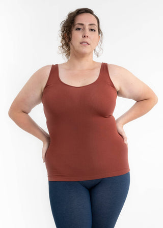 Woman wearing rust-colored fitted tank top with hands on hips against white background