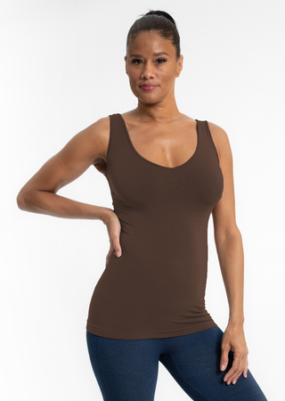 Woman wearing brown fitted tank top with scoop neckline and blue leggings against white background.