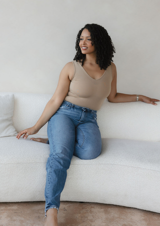 Woman wearing beige reversible cami top with jeans, sitting relaxed on white couch