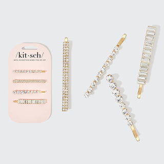 Four gold rhinestone bobby pins with crystal embellishments displayed next to pink packaging