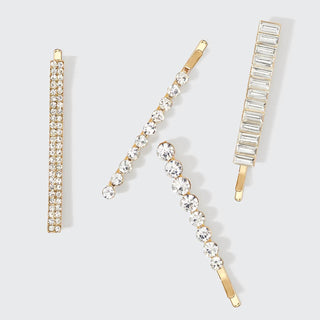Four gold-toned bobby pins with crystal rhinestones in different patterns arranged on white background