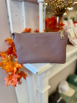 Mauve leather crossbody wristlet bag displayed on white ladder shelf with autumn leaves and home decor