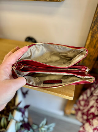 Hand holding open red crossbody bag showing multiple zippered compartments with cream fabric lining