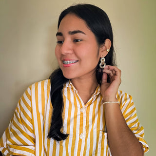 Young woman wearing circular ripple design gold earrings with yellow striped shirt, smiling at camera.