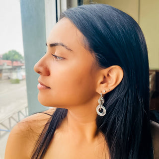 Woman in profile wearing silver ripple drop earrings with circular design and small stud earrings.
