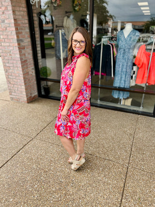 Woman wearing floral sleeveless mini dress standing outside clothing boutique storefront
