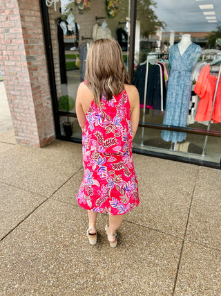 Woman wearing pink floral sleeveless mini dress standing outside clothing boutique storefront
