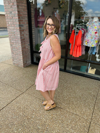 Woman wearing pink and white striped sleeveless linen dress standing outside boutique storefront.