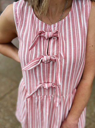 Woman wearing red and white striped sleeveless dress with decorative bow ties down the front.