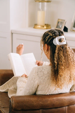 Woman reading book wearing white round flat hair clip in curly blonde hair