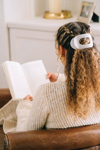 Woman reading book with white round hair clip holding back curly blonde hair