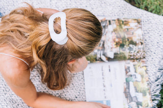 Woman wearing white round hair clip in messy bun while reading magazine outdoors