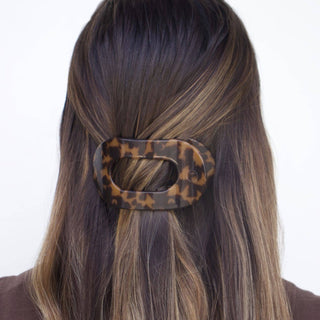 Woman wearing tortoiseshell hair clip with oval opening securing brown highlighted hair in half-up style
