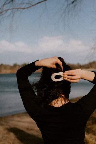 Person styling hair with small round flat hair clip in natural outdoor setting