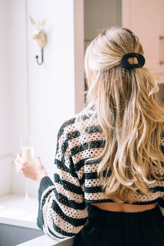 Woman with blonde wavy hair wearing a black round hair clip in half-up hairstyle.