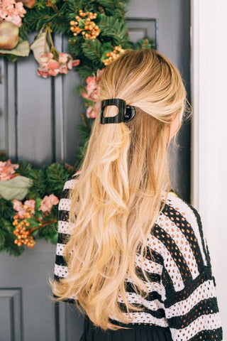Woman with blonde wavy hair wearing a black round flat hair clip in half-up hairstyle.