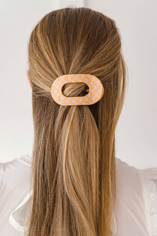 Woman wearing oval polka dot hair clip in blonde hair, back view showing hairstyle accessory.