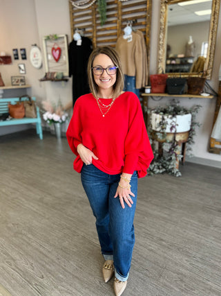 Woman wearing red relaxed dolman sweater with jeans and accessories in boutique setting
