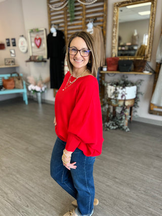 Woman wearing red relaxed dolman sweater with jeans standing in boutique interior