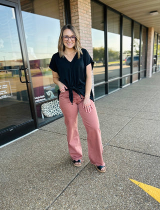 Woman wearing black top and rust-colored vintage flare jeans standing outside storefront