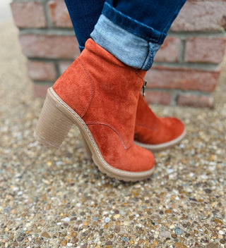 Rust faux suede ankle boots with block heels worn with jeans on gravel surface