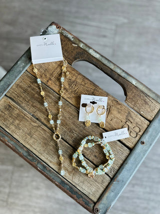 Simply Noelle sage green and gold beaded necklace, hoop earrings, and bracelet set displayed on rustic wooden crate.