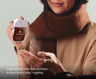 Woman spraying Touchland Power Mist hand sanitizer into her palm while wearing a cozy scarf.