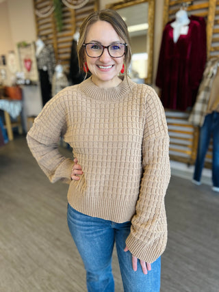 Woman wearing beige textured knit sweater with jeans in clothing store setting